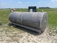 A horizontal gray fuel storage tank sitting on a grassy field under a clear blue sky.