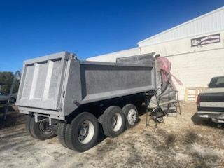 A grey dump truck trailer sits on gravel outside a white building under a clear blue sky.