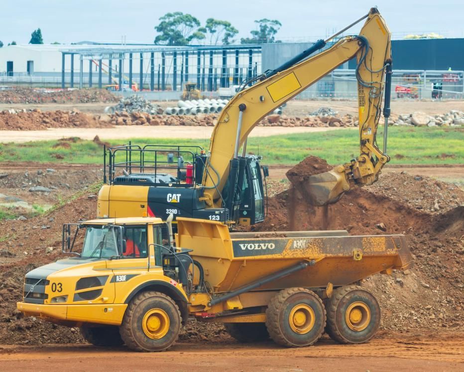 A Volvo Dump Truck is Being Loaded With Dirt by a Cat Excavator — Lohman Contracting in Emerald, QLD
