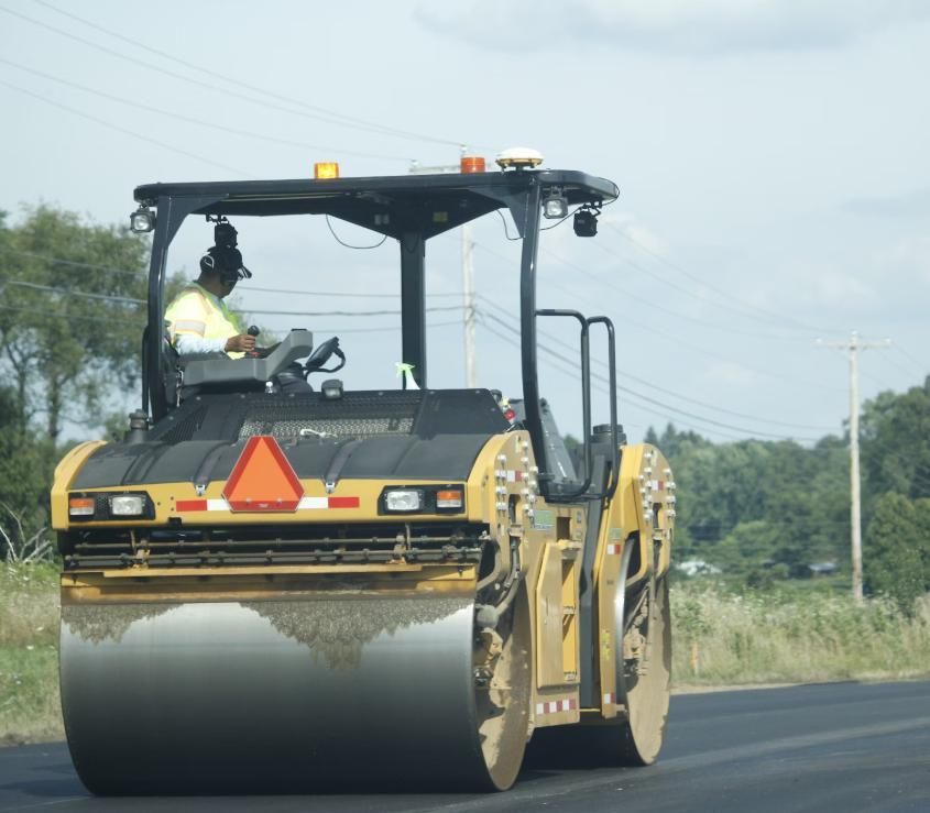 A Man is Driving a Yellow and Black Roller on a Road — Lohman Contracting in Emerald, QLD