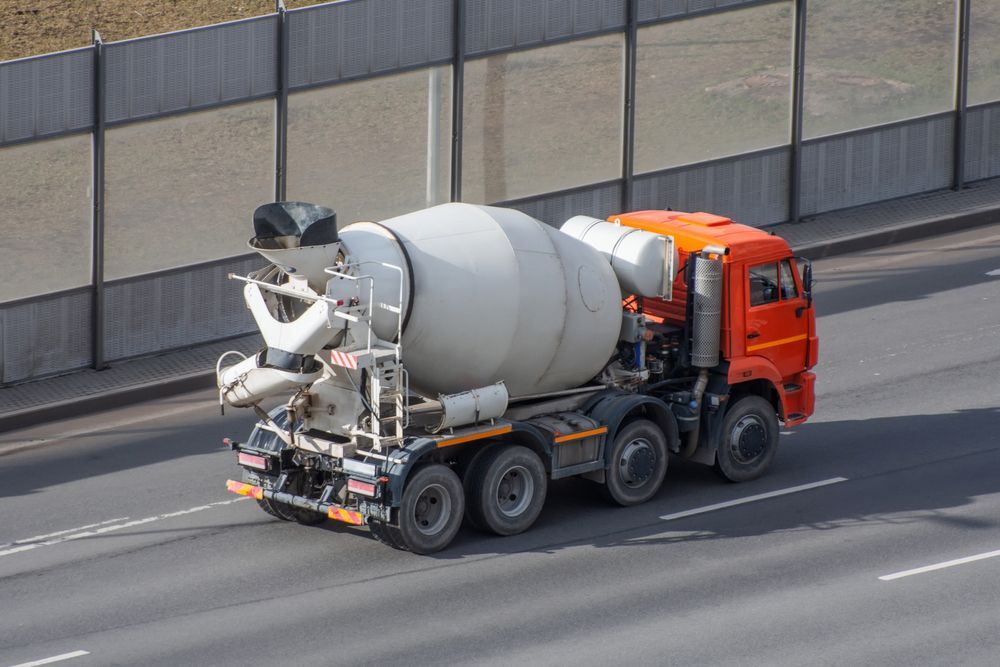 Orange Cement Mixer Truck Driving on a Highway Beside a Concrete Barrier — Lohman Contracting in Emerald, QLD