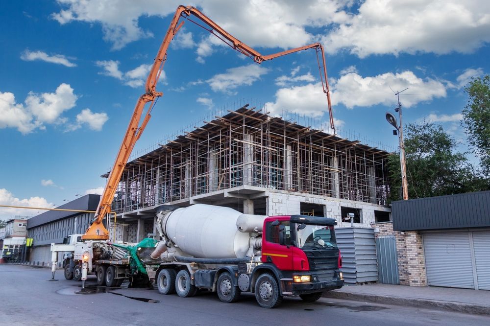 Concrete Truck at Construction Site Beneath an Orange Boom Pump Beside a Building Under Construction — Lohman Contracting in Emerald, QLD
