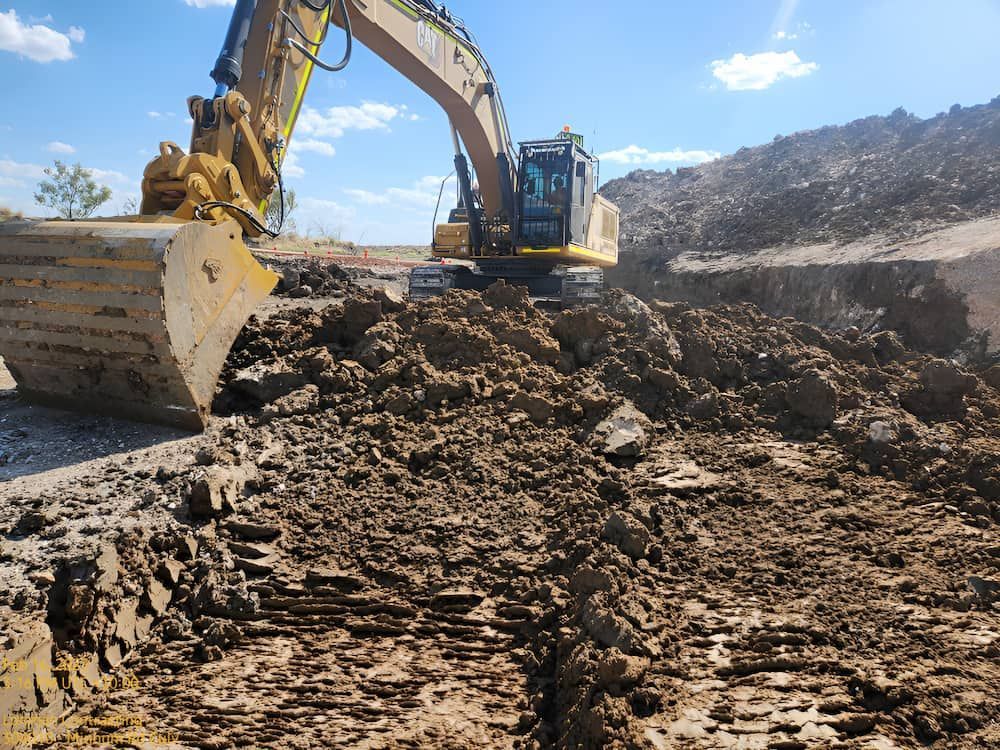 A Large Excavator Is Moving Dirt In A Muddy Field — Lohman Contracting in Biloela, QLD