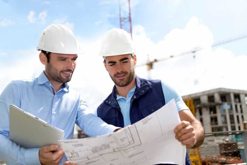 Two Construction Workers Are Looking At A Blueprint At A Construction Site — Lohman Contracting in Emerald, QLD