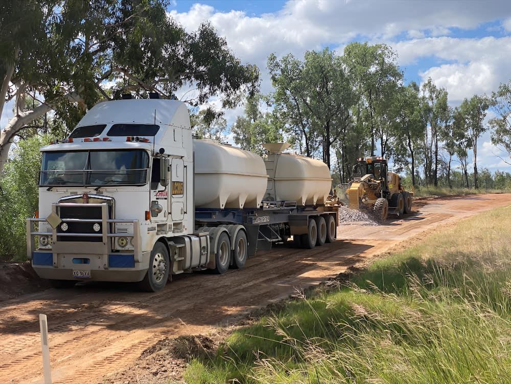 A Semi Truck Is Driving Down A Dirt Road Next To A Bulldozer — Lohman Contracting in Emerald, QLD