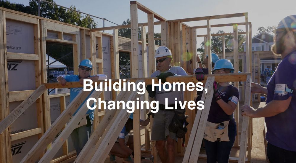 People building a house frame; sunny outdoor setting. Text: Building Homes, Changing Lives.