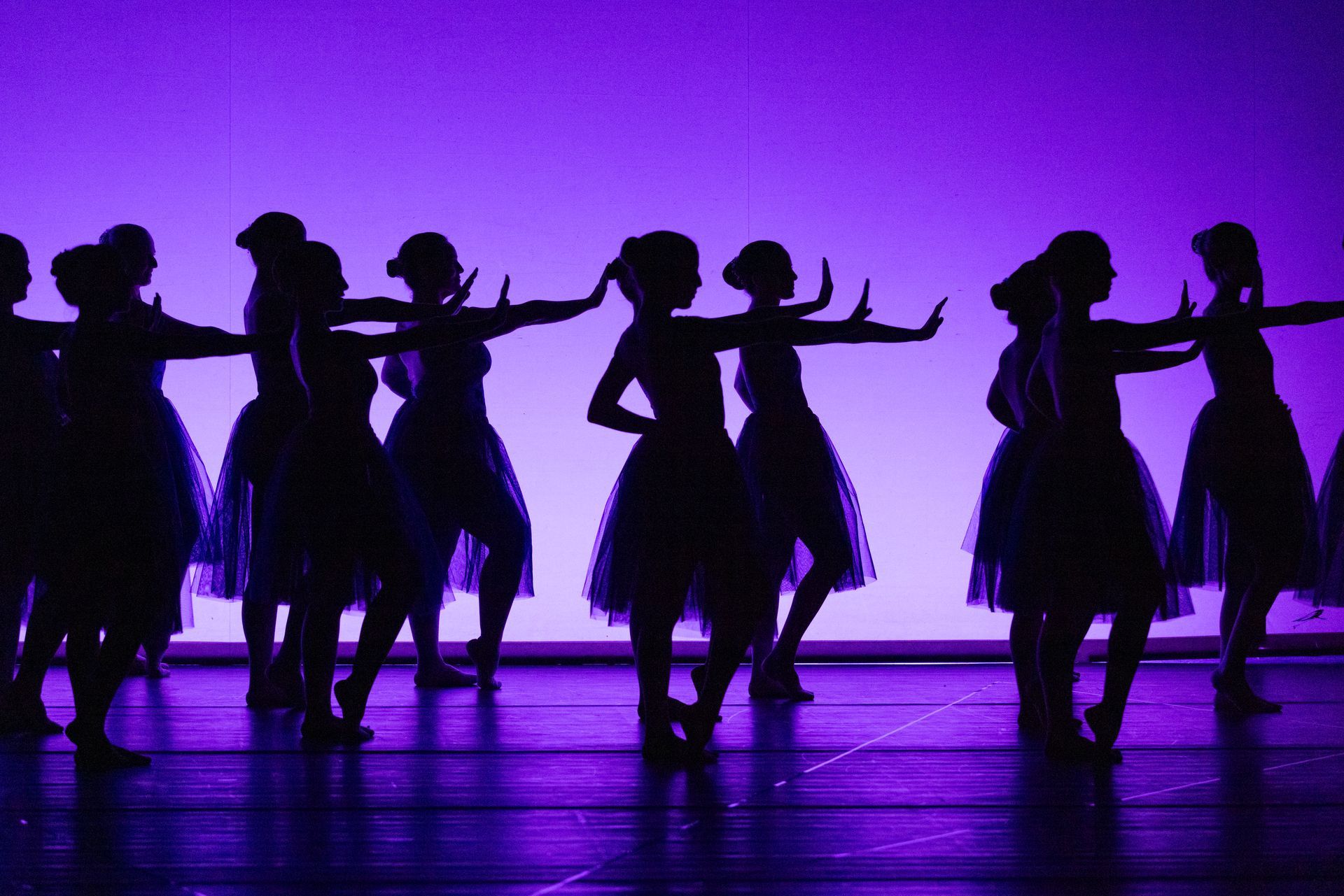 Un grupo de chicas jóvenes bailan en un escenario frente a un fondo morado.