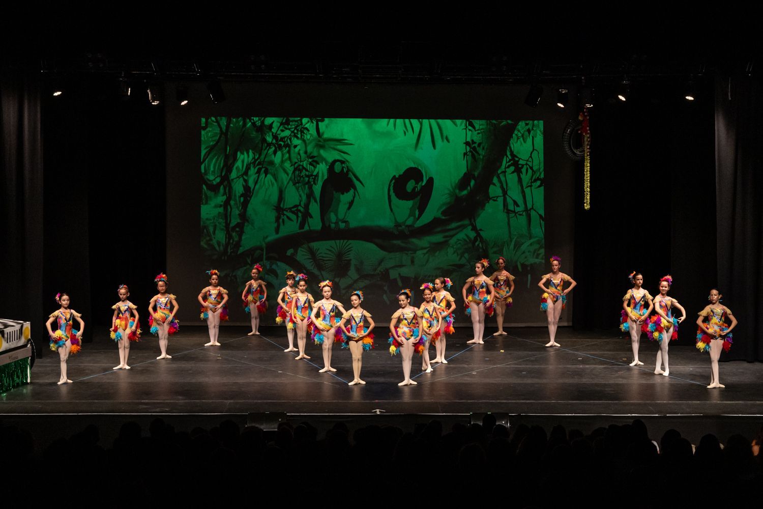 Un grupo de chicas jóvenes bailan en un escenario frente a una pantalla grande.