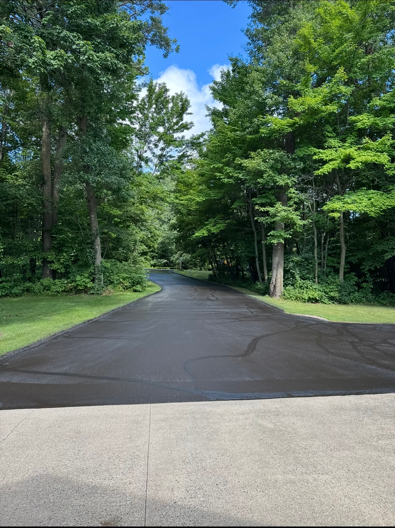 Paved road curving through a green wooded area under a blue sky