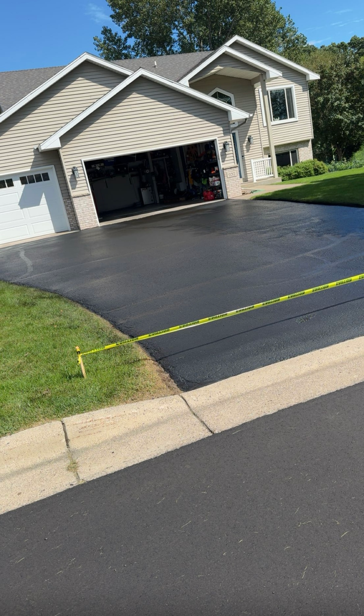 Suburban house with a freshly sealed black driveway and open garage on a sunny day
