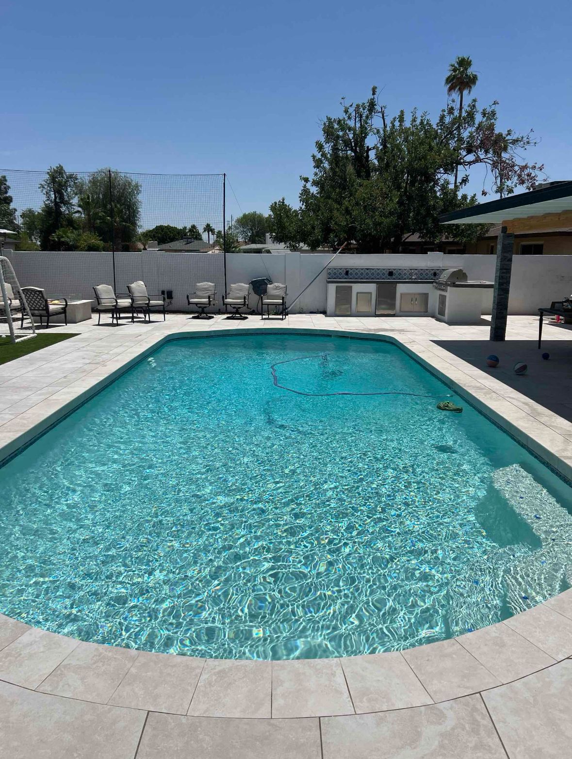 A rectangular swimming pool with clear turquoise water in a sunny backyard.