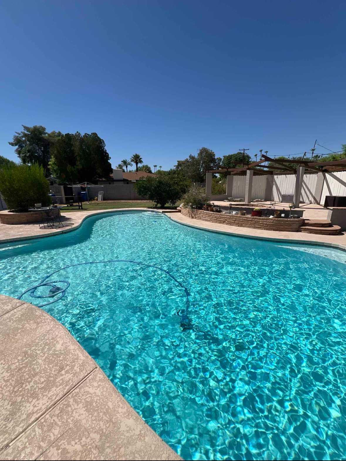 A turquoise pool in a backyard under a clear blue sky on a sunny day.