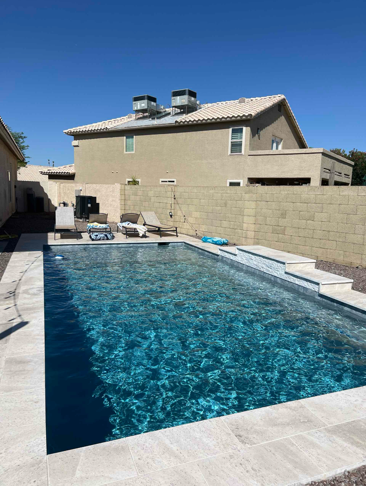 A backyard pool in front of a two-story house, with lounge chairs and a clear, blue sky overhead.