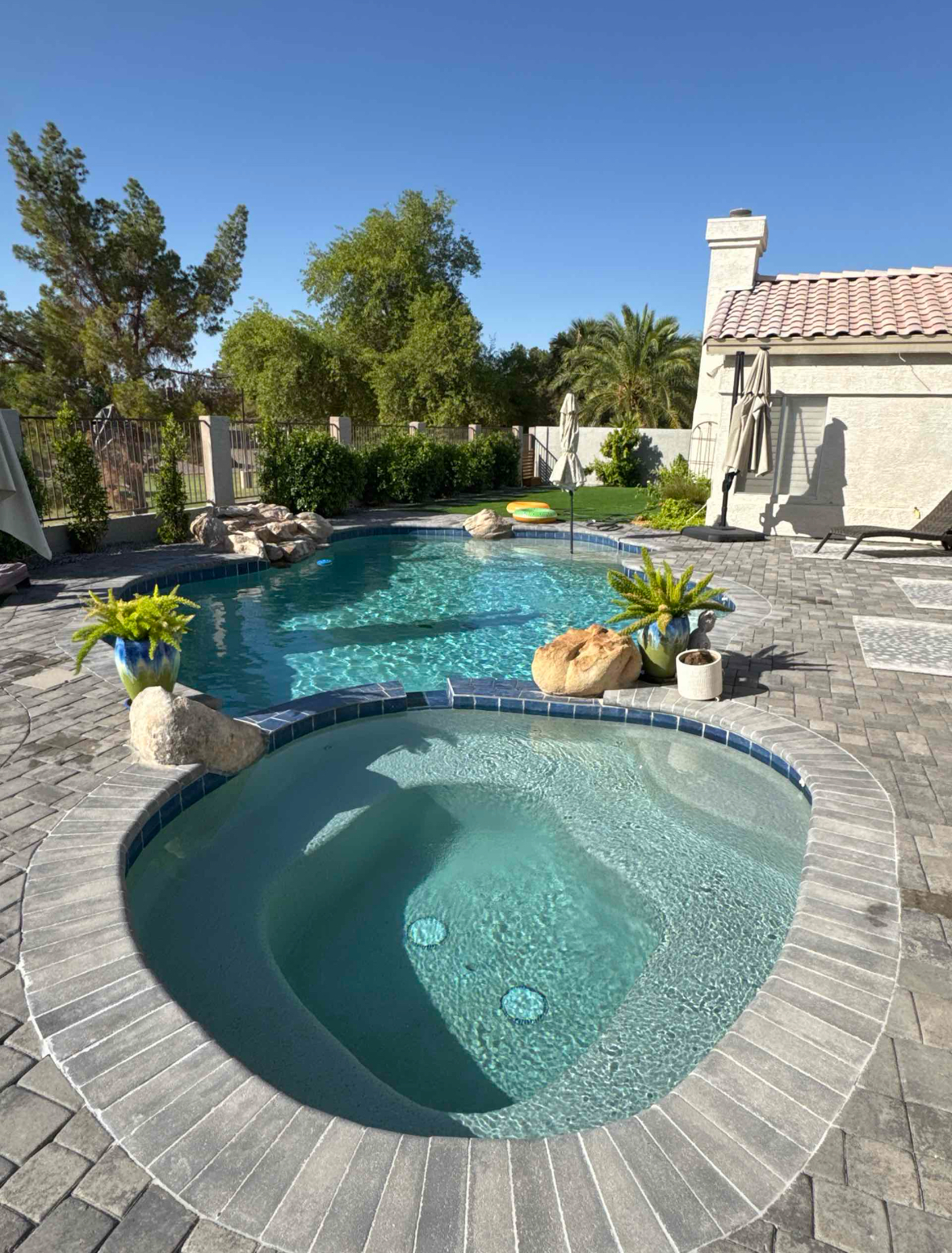 Pool and spa in a backyard, surrounded by pavers, with blue water and blue skies.