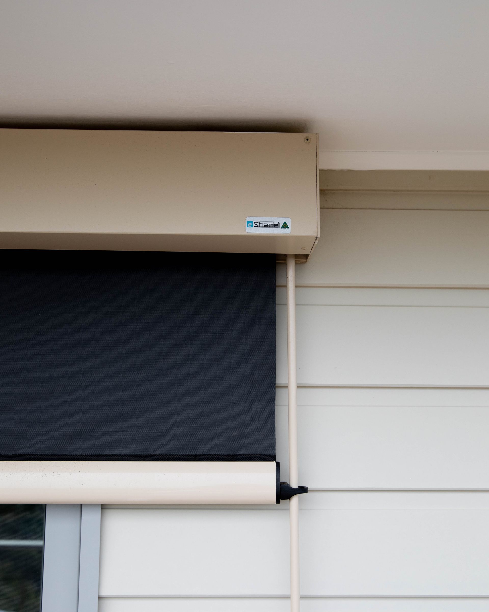 Beige roller shutter box above a dark mesh blind partially rolled down.