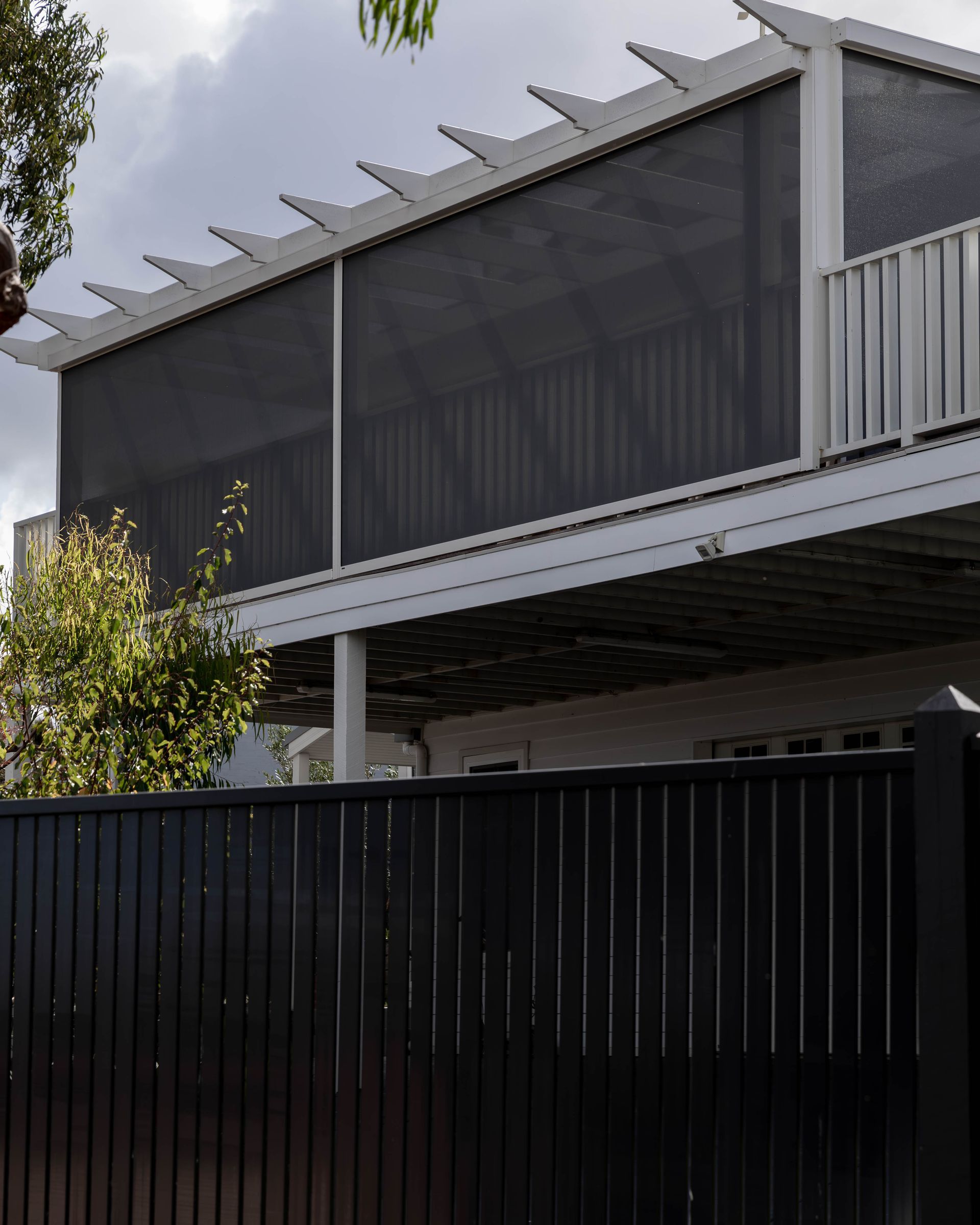 Dark grey mesh screen covering a white pergola on a two-story building, set behind a black fence.