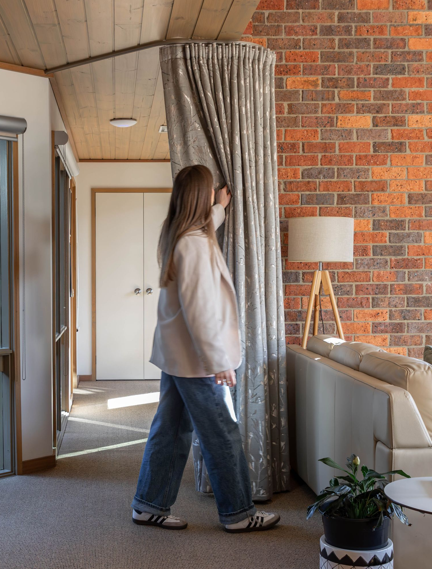 Woman pulling back a shimmering curtain in a room with a brick wall and a sofa.