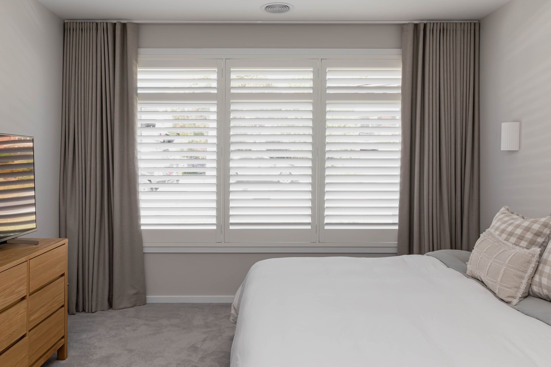 Bedroom with a window featuring white shutters, gray curtains, and a bed with white bedding.