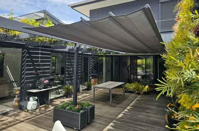Backyard patio with retractable shade awning, table, plants, and black modern home.