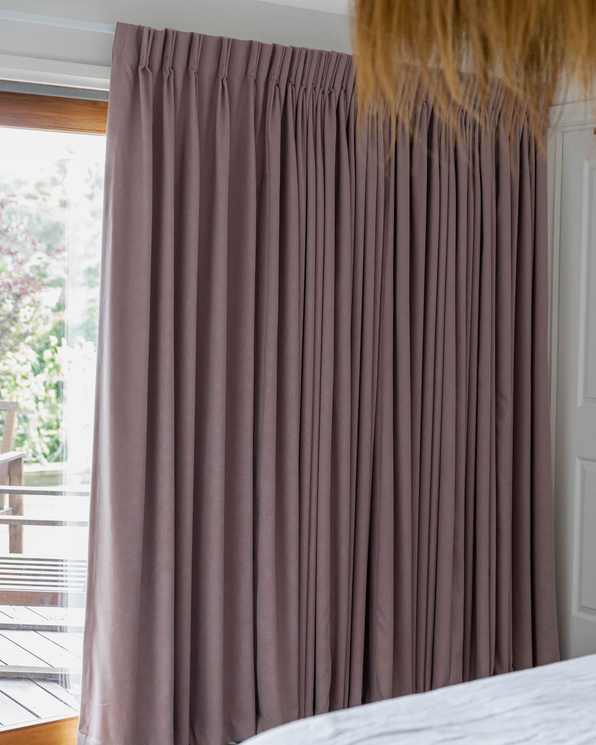 Mauve pleated curtains covering a doorway, partially obscuring a view of a balcony.