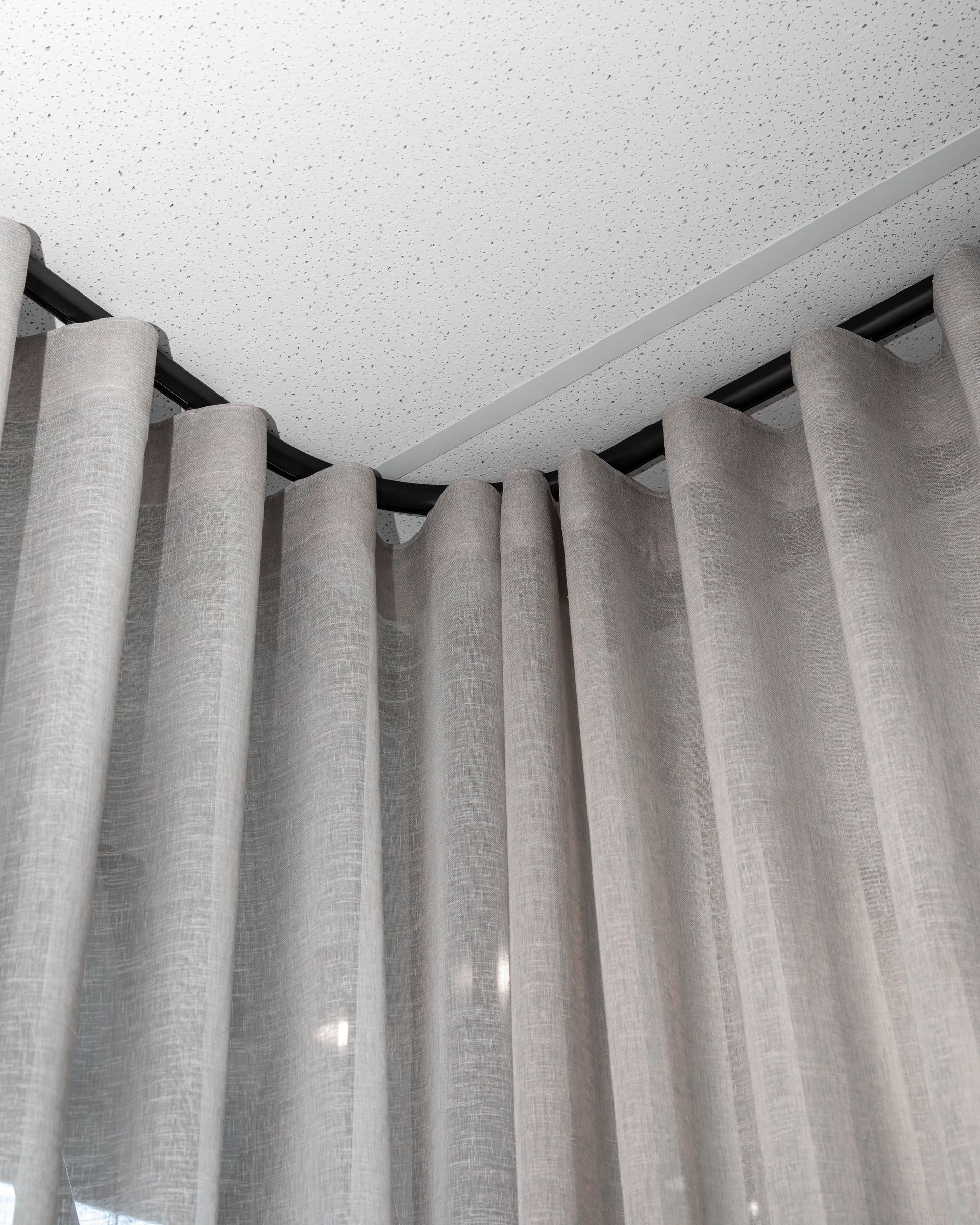 Curtains hanging from a curved black rod at a corner, light gray fabric, ceiling visible.