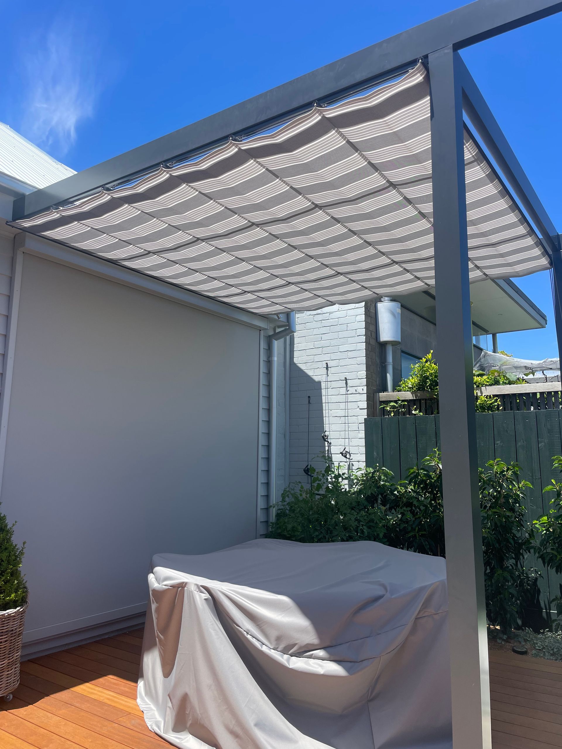 A modern outdoor seating area with a retractable fabric shade and a covered table on a wooden deck.