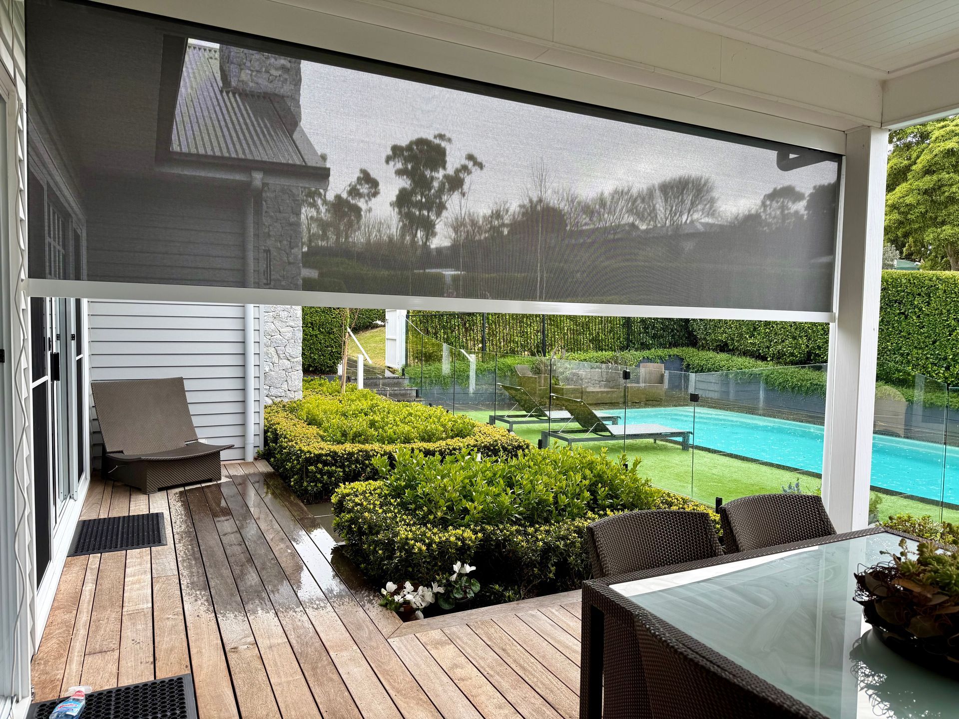 Outdoor patio with shade screen, overlooking a backyard with pool and hedges.