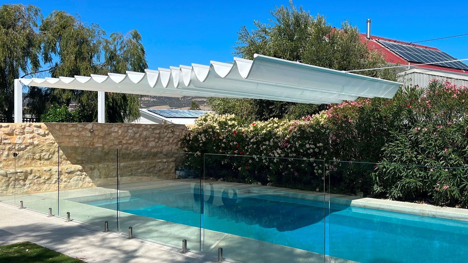 Pool with white shade structure over the top, set against a backdrop of trees and a clear blue sky.
