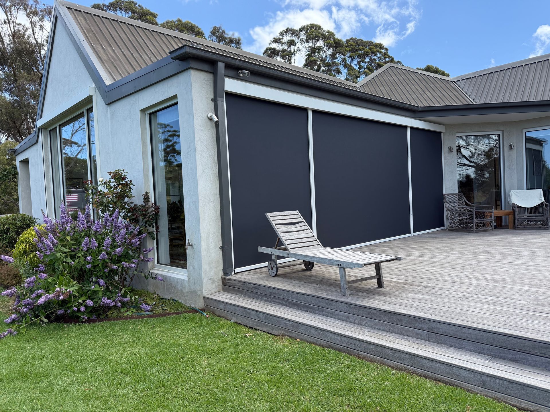 Exterior of house with black sunscreens, a chaise lounge, and lush greenery.