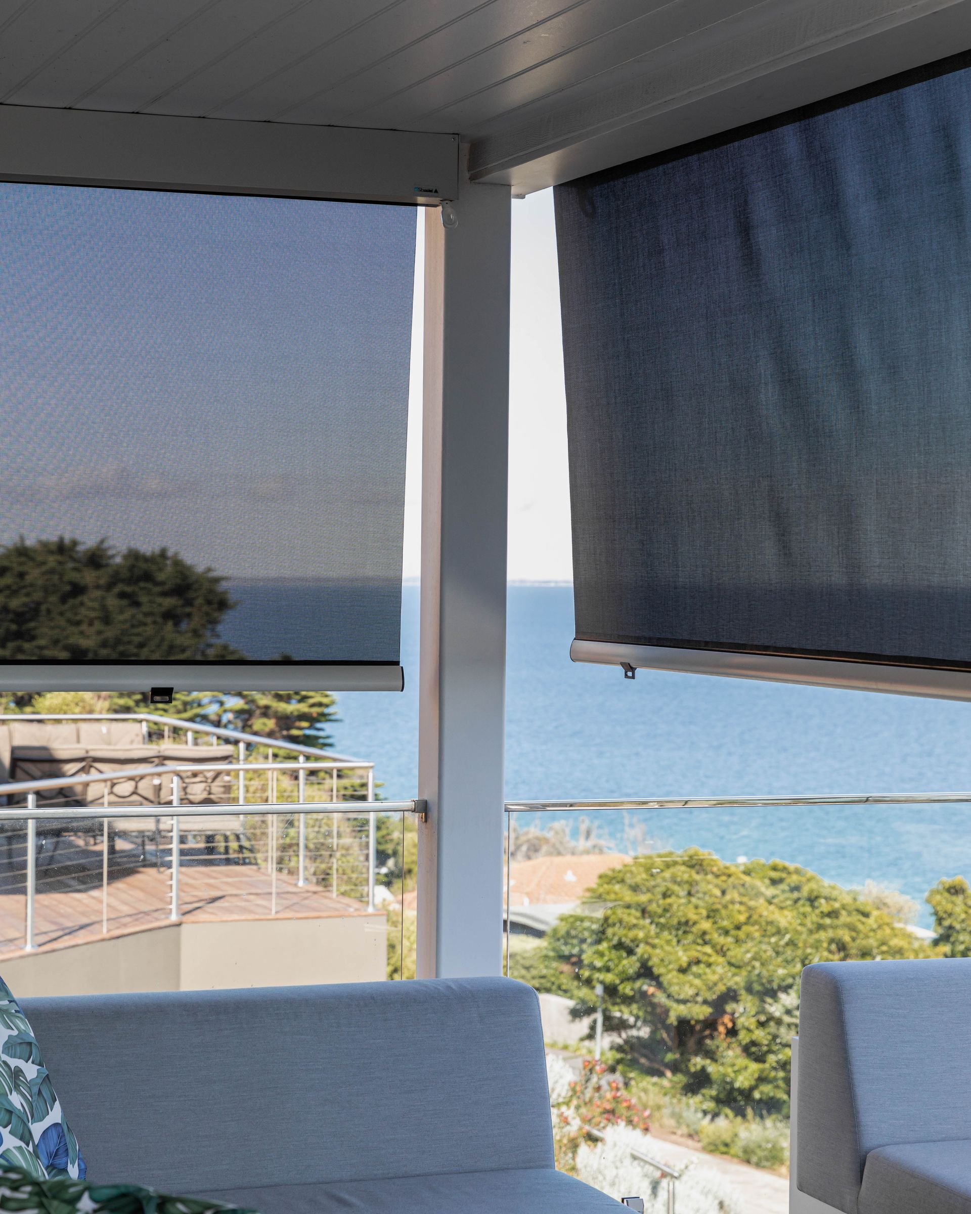 Two outdoor sun shades on a white-columned patio overlooking the ocean and trees.