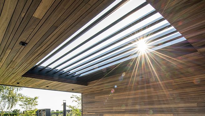 Wooden pergola roof with retractable slats, sunlight streaming through, outdoor setting.