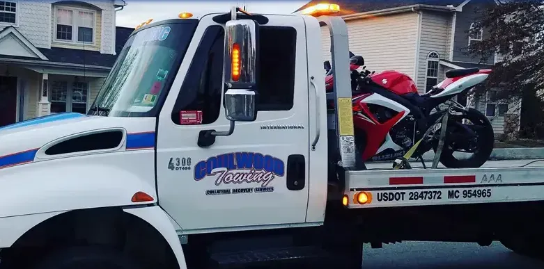 A white flatbed tow truck carries a red and white sport motorcycle on its rear platform.