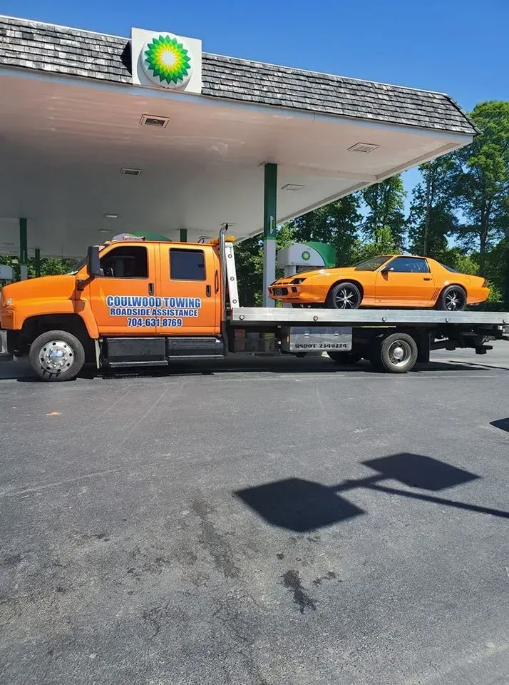 An orange tow truck carries an orange sports car, parked under the canopy of a BP gas station.