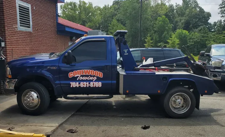 A dark blue Calwood Towing tow truck parked in a gravel lot next to a brick building.