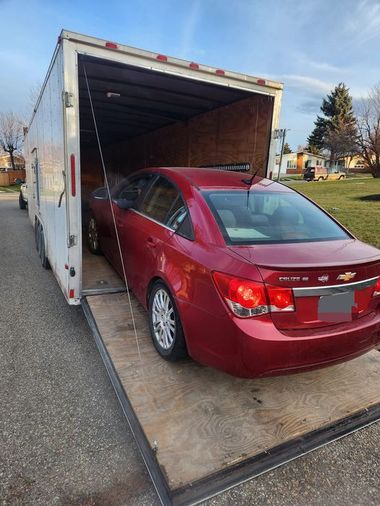 Red sedan loaded in an open white moving truck on a roadside
