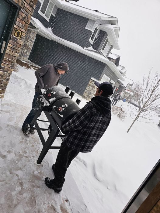 Two people grilling outdoors in snowy weather beside a house