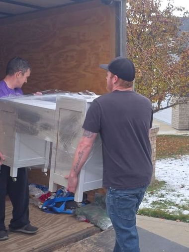 Two men loading a large white cabinet into a moving truck on a wooden ramp.