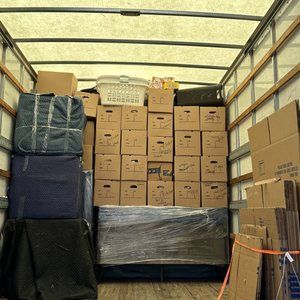 Packed boxes stacked inside the back of a moving truck with covered furniture.