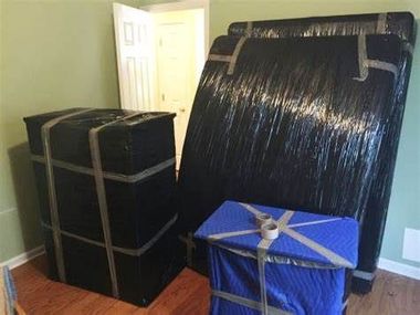 Packed furniture wrapped in black and blue plastic in a room near a doorway