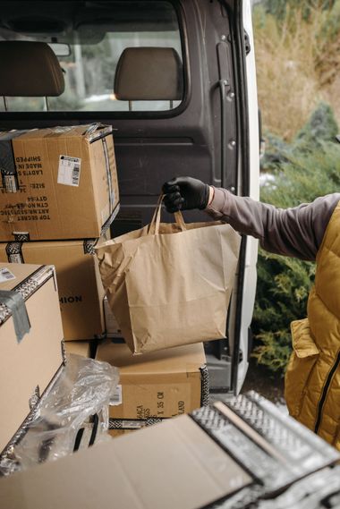 Person unloading cardboard boxes and a paper grocery bag from a van.
