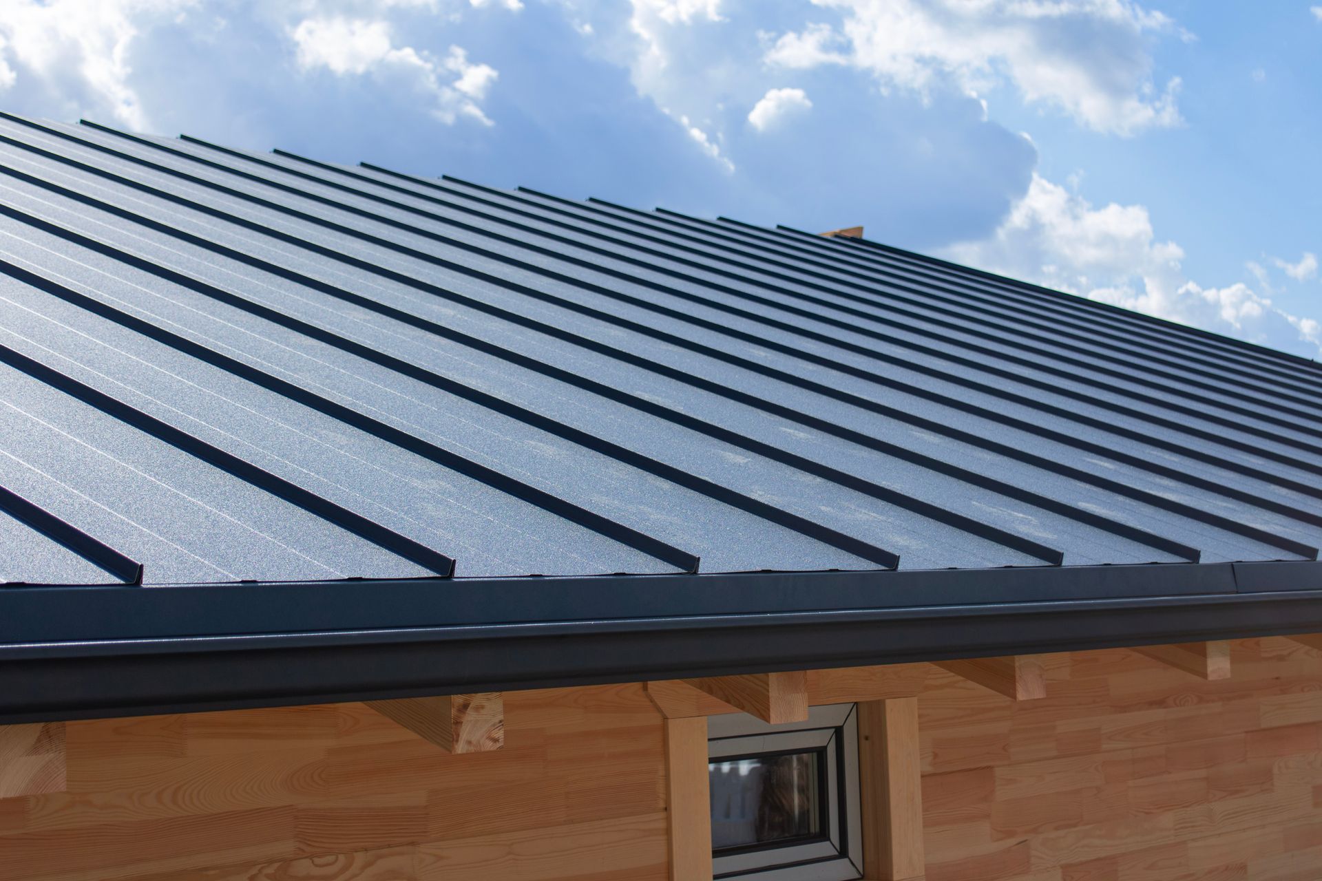 Blue metal roof on a house under a partly cloudy sky