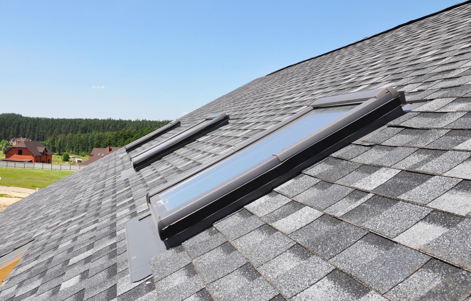 Roof with two skylights on gray shingles under a clear blue sky