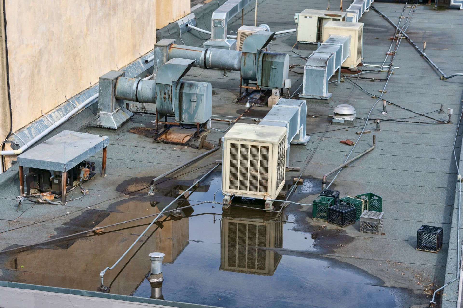Rooftop HVAC units and vents beside a wall, with puddles reflecting the equipment.