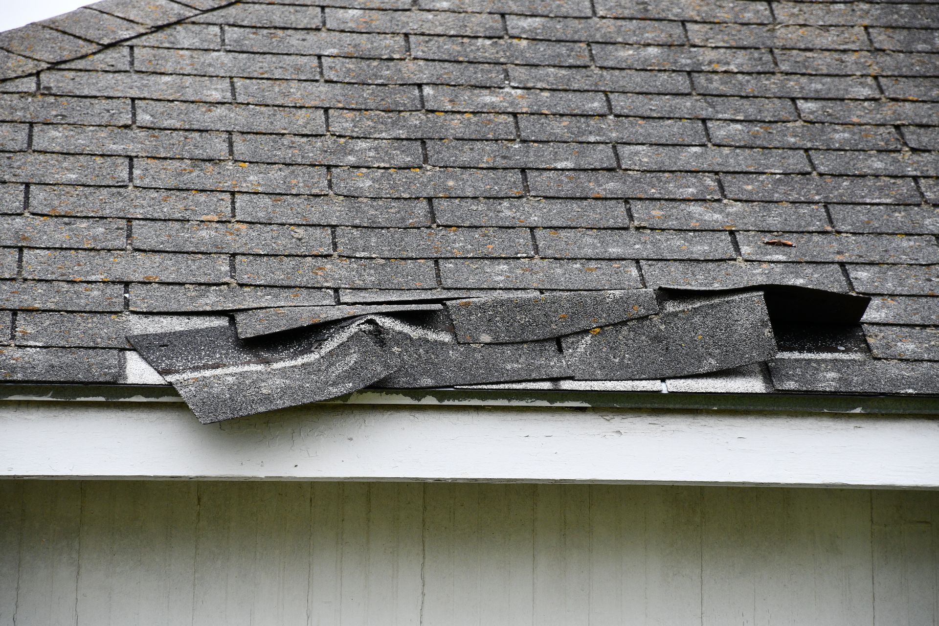 Damaged roof shingles with a torn section and exposed edge above a building exterior