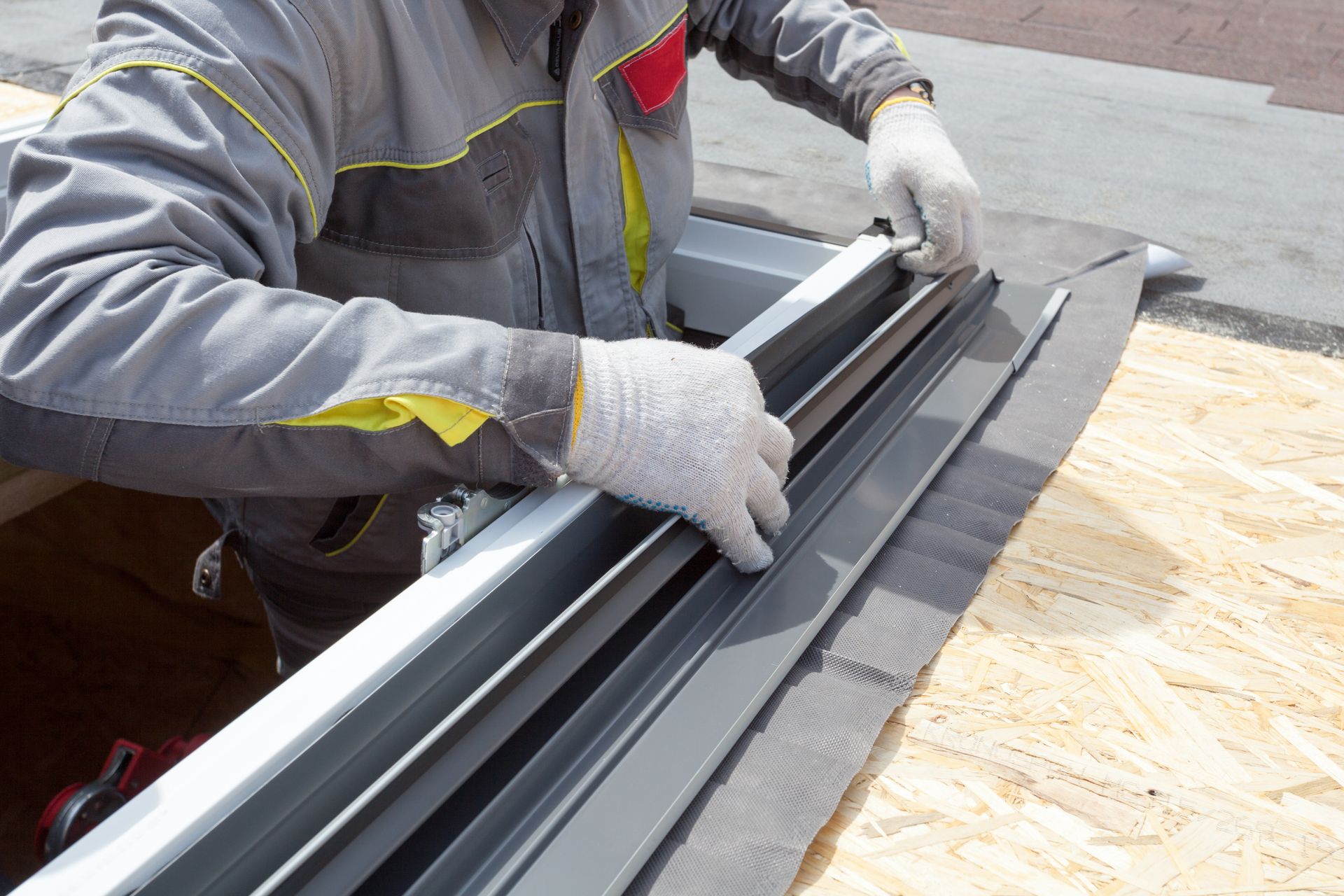 Worker in gray gloves handling black trim strips on a plywood work surface outdoors
