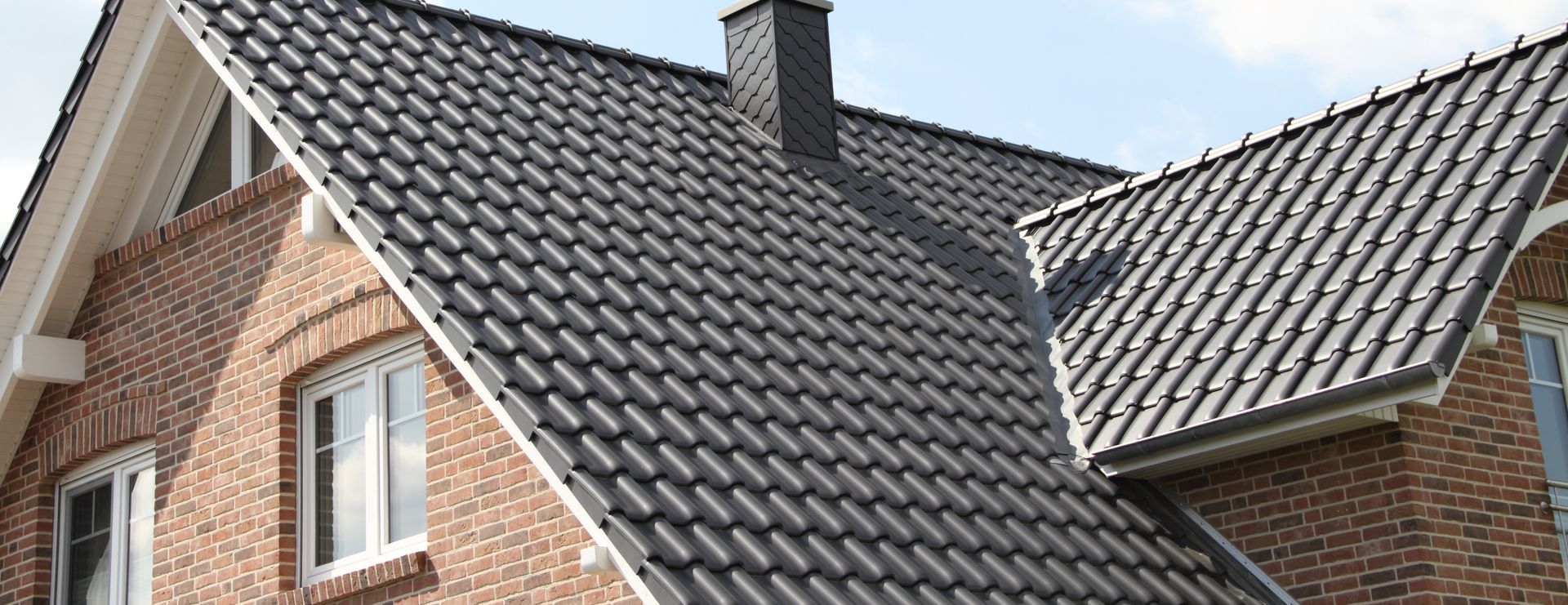 Brick house with steep gray tiled roof and dormer windows under a cloudy sky