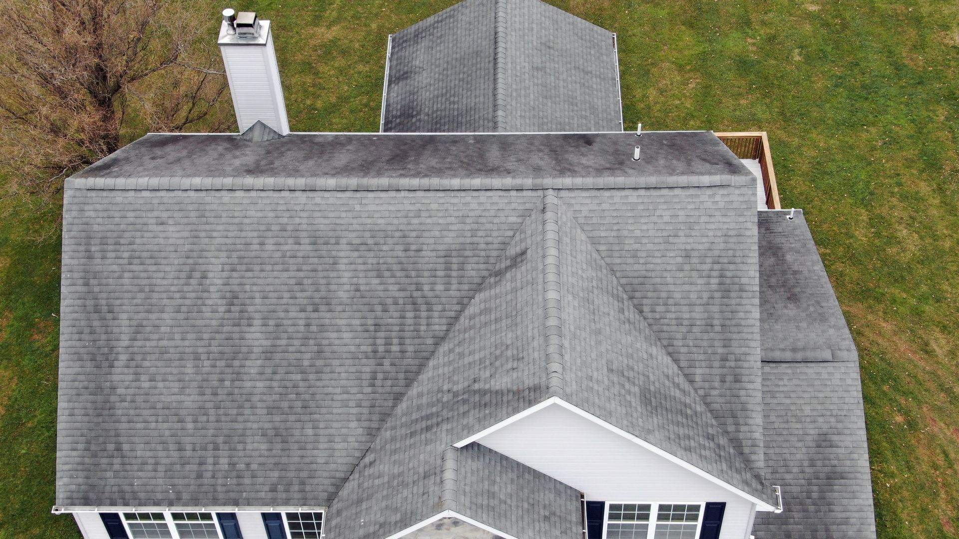 Aerial view of a gray-roofed house with a chimney and dormer windows, surrounded by grass.