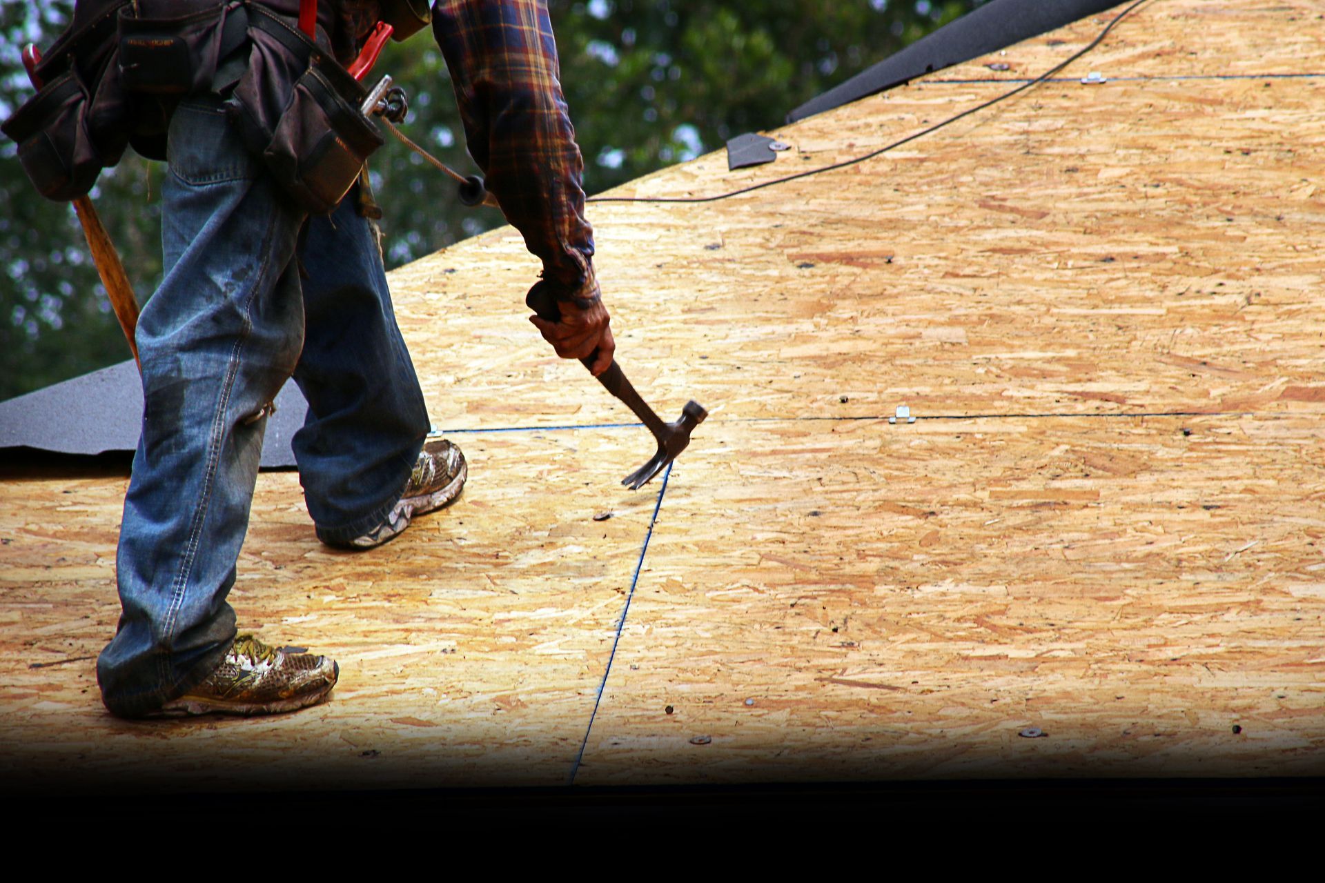 Worker using a hammer to nail plywood roofing on a roof deck
