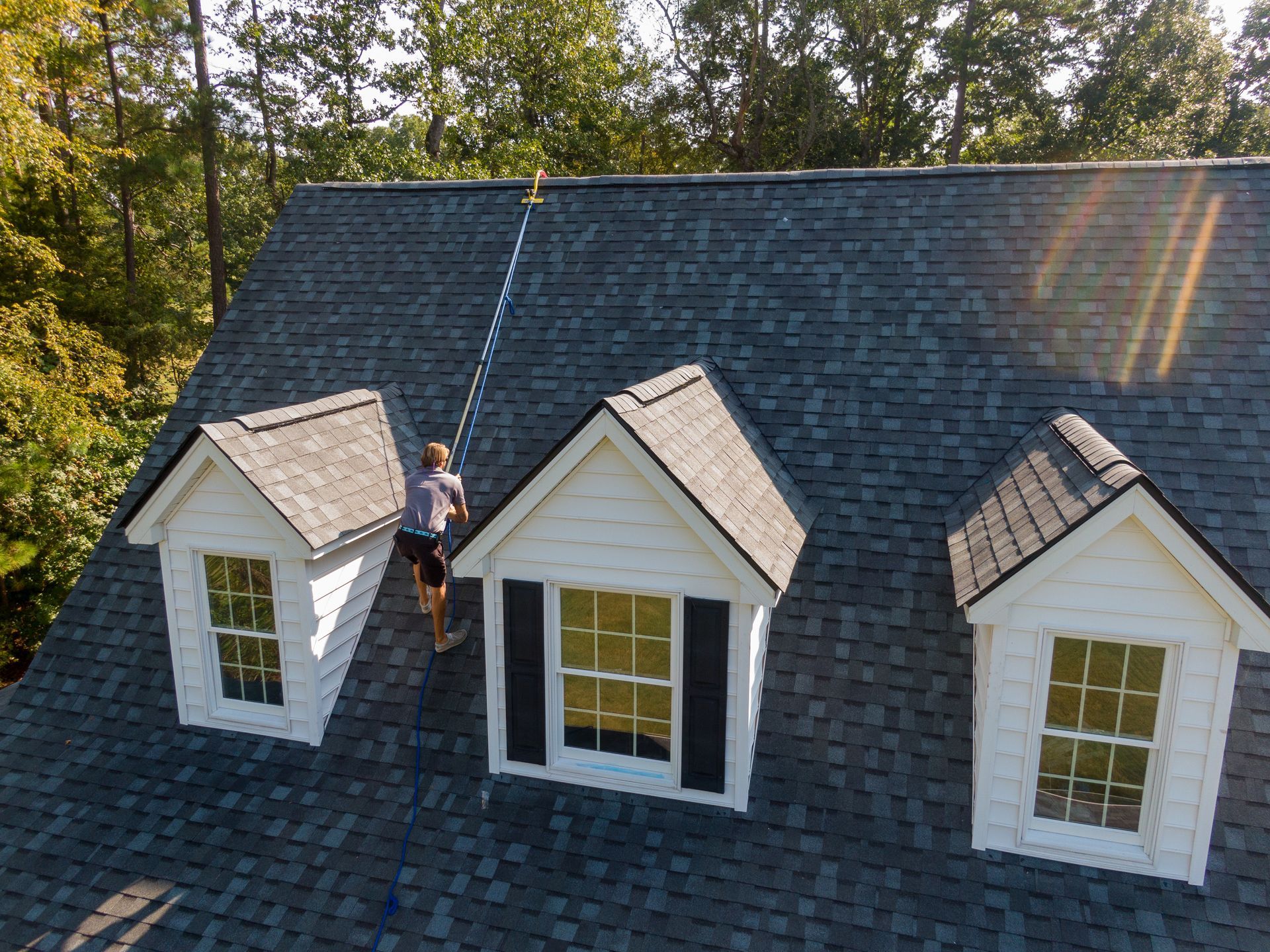 Worker on a gray shingled roof installing a skylight between three dormer windows on a house