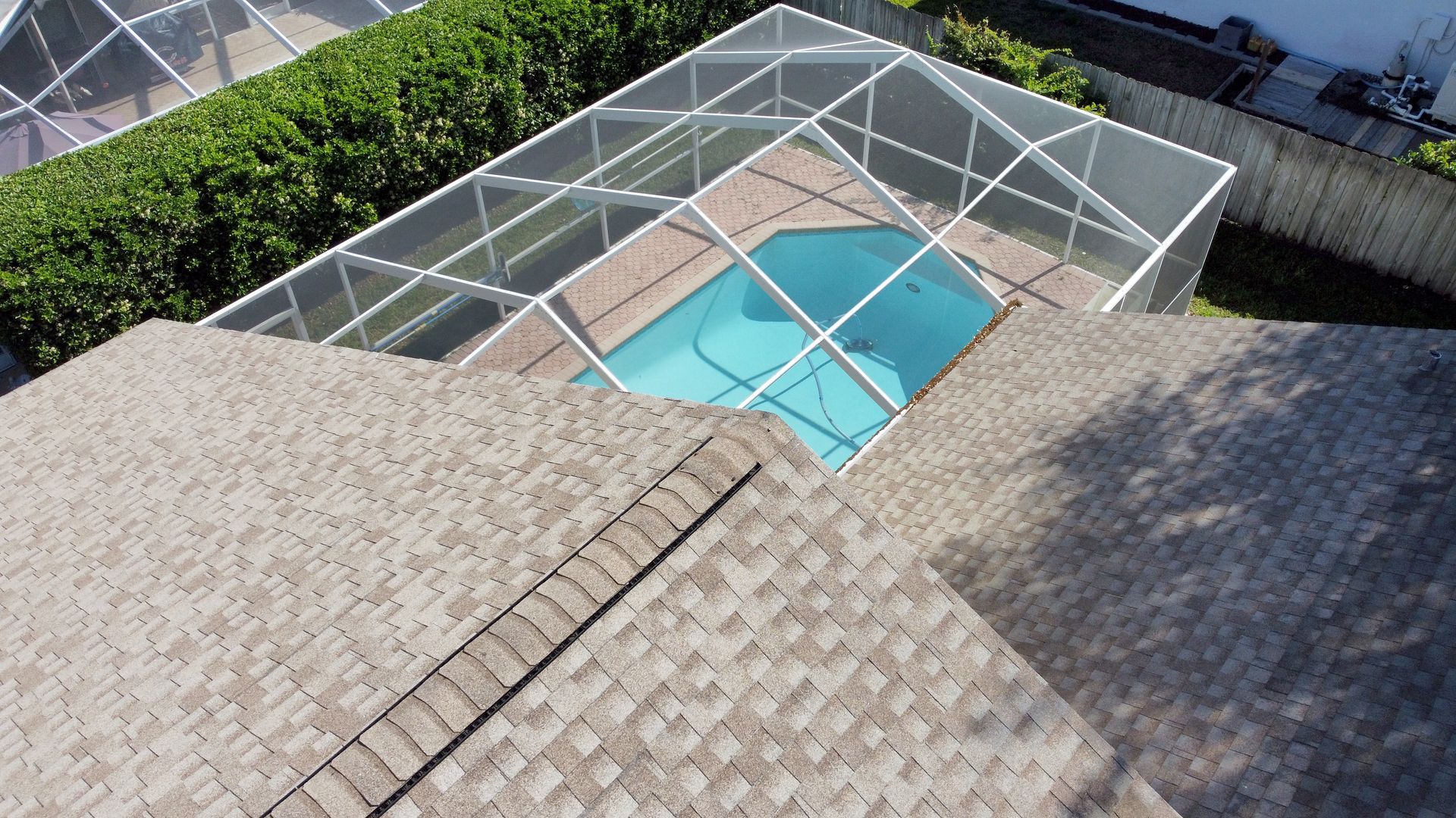 Backyard pool enclosed by a white screened patio beside a shingled roof
